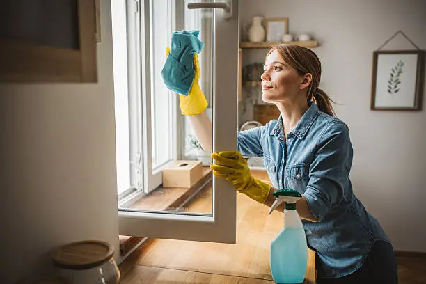 Cleaner removing water spots from coastal home windows before afternoon guests arrive